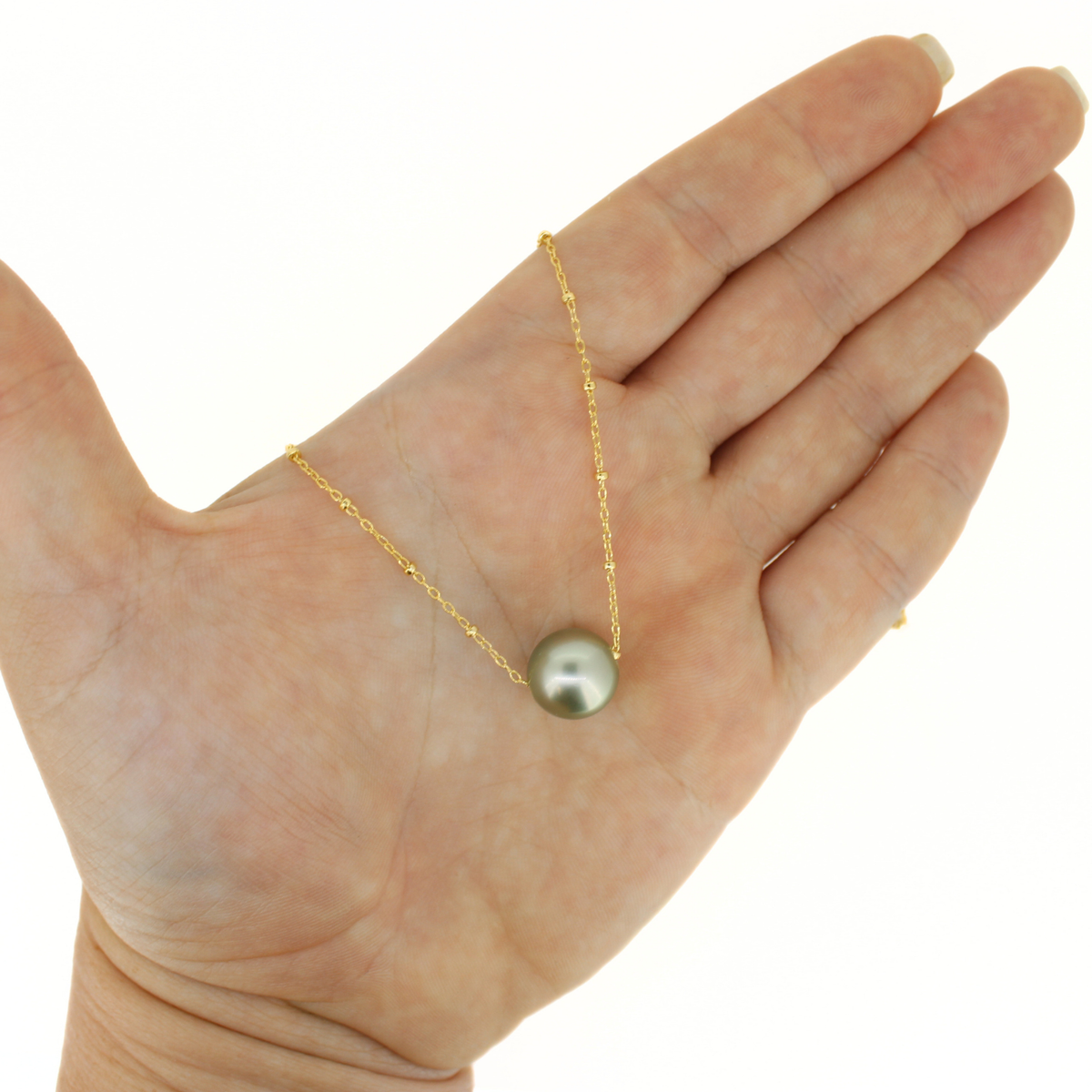A gold chain necklace with a single round gray pearl pendant, held in the center of an open hand against a plain white background.