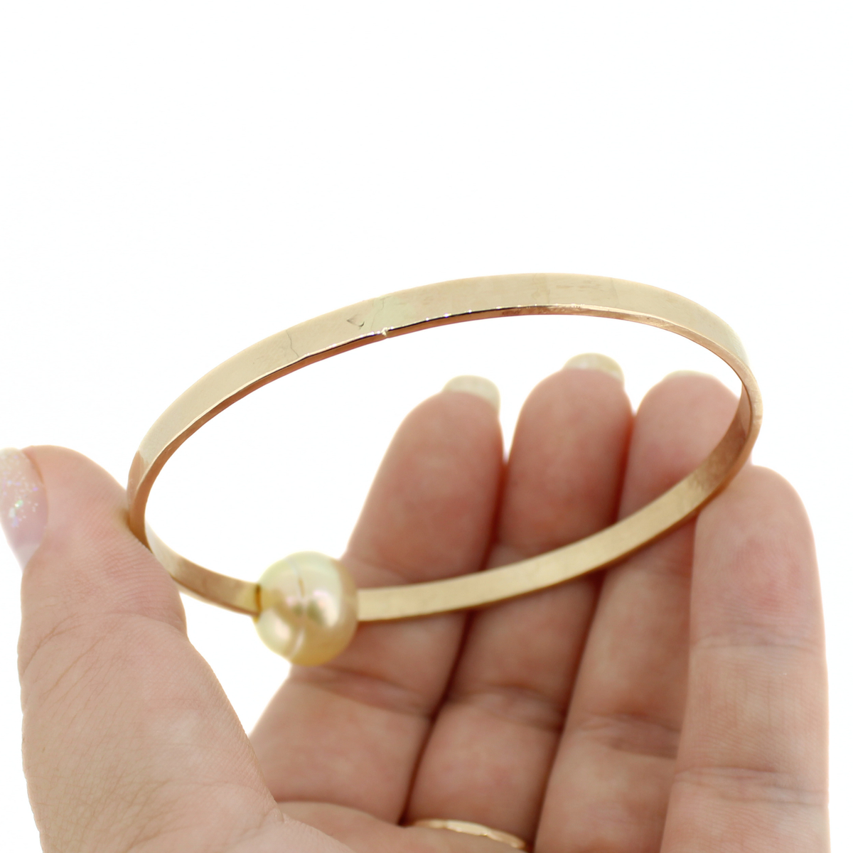 Gold bangle bracelet showing it's hammered texture agains a white background