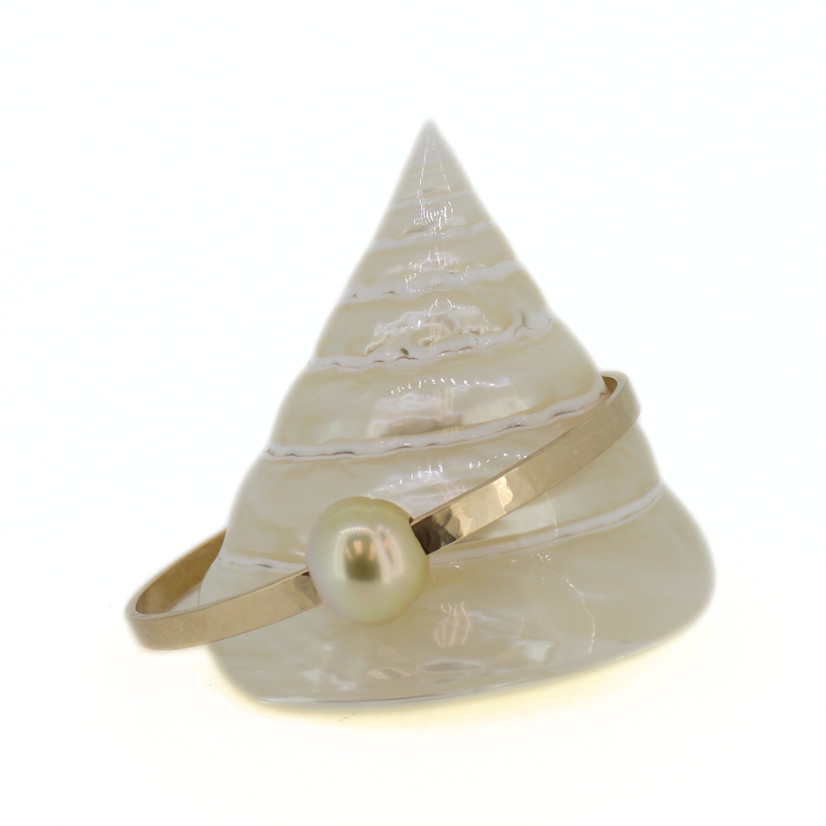 A gold metal bangle bracelet with a single round pearl, displayed on a white seashell jewelry stand against a white background.