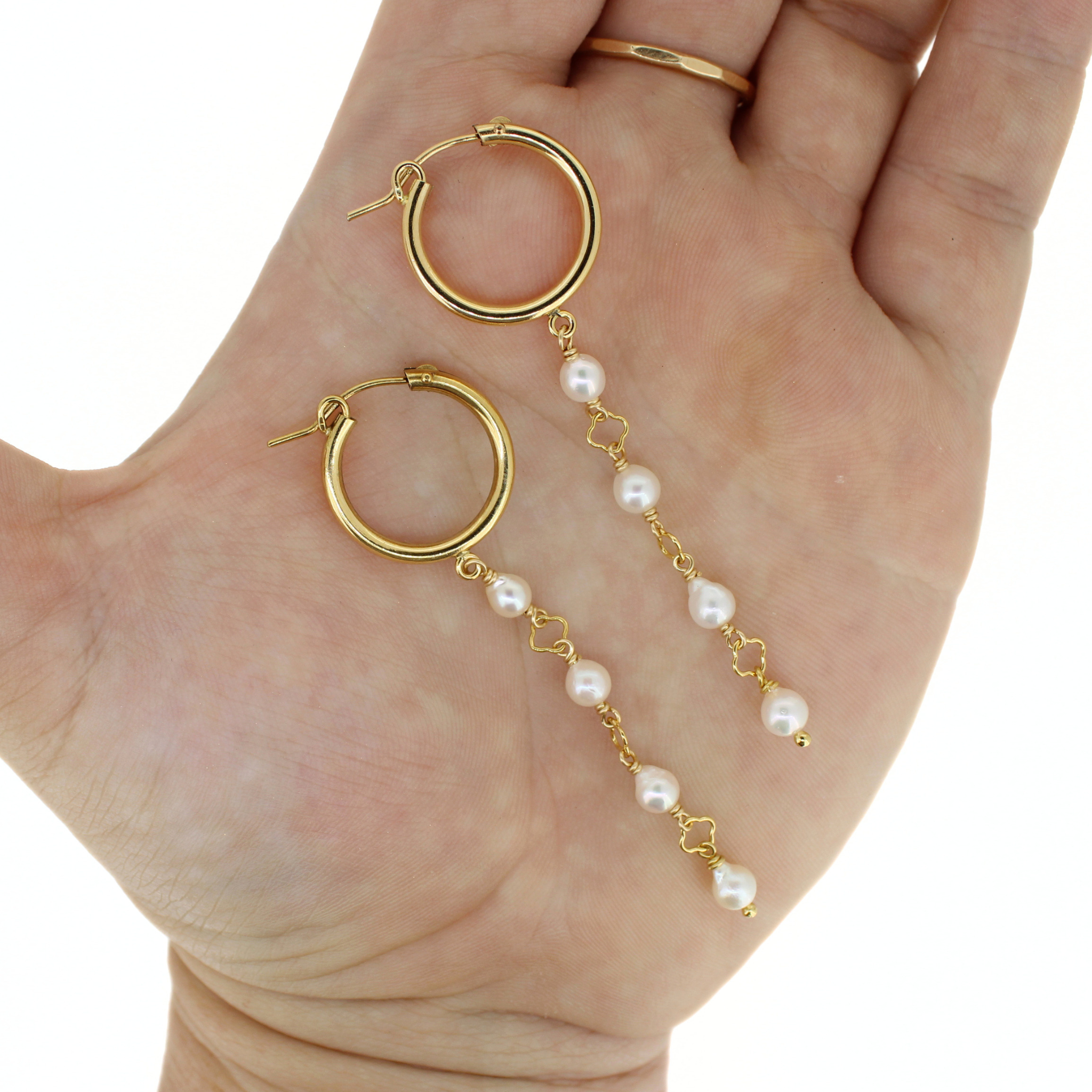 Gold hoop dangle earrings with white freshwater pearls, displayed on a person's palm hand against a white background.
