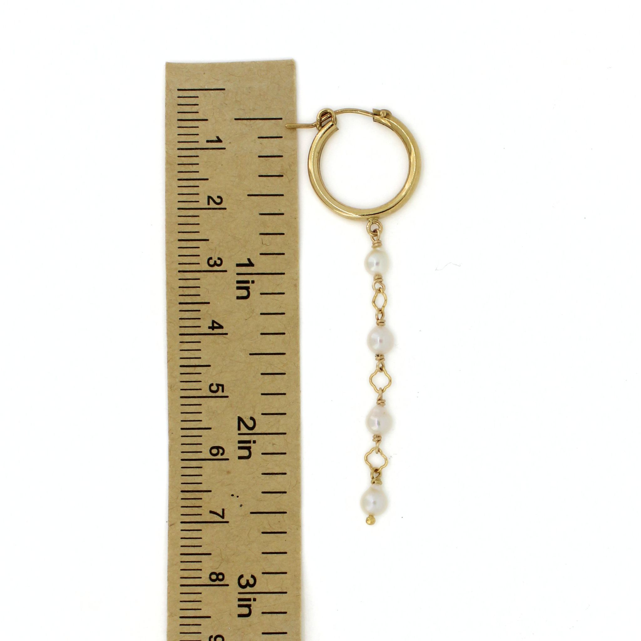 A single gold hoop earring with a dangling chain of white pearls and small gold links, shown next to a ruler for scale on a white background.