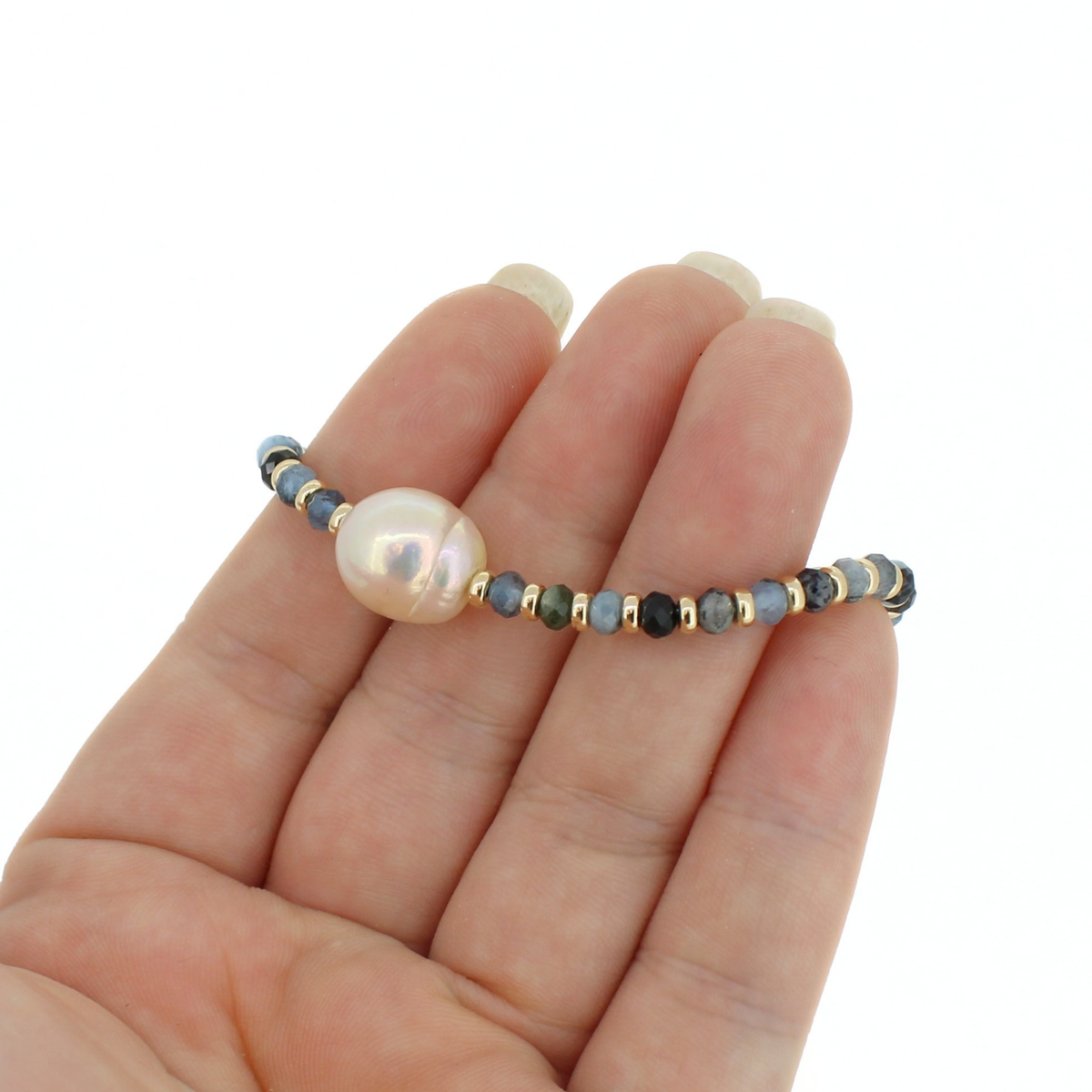 A beaded bracelet with a large lustrous pearl and small faceted beads, shown resting on a person's hand against a plain white background.