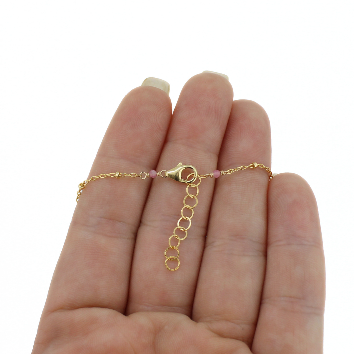 A delicate gold chain necklace with a lobster clasp and small pink beads, shown resting on an open hand against a white background.