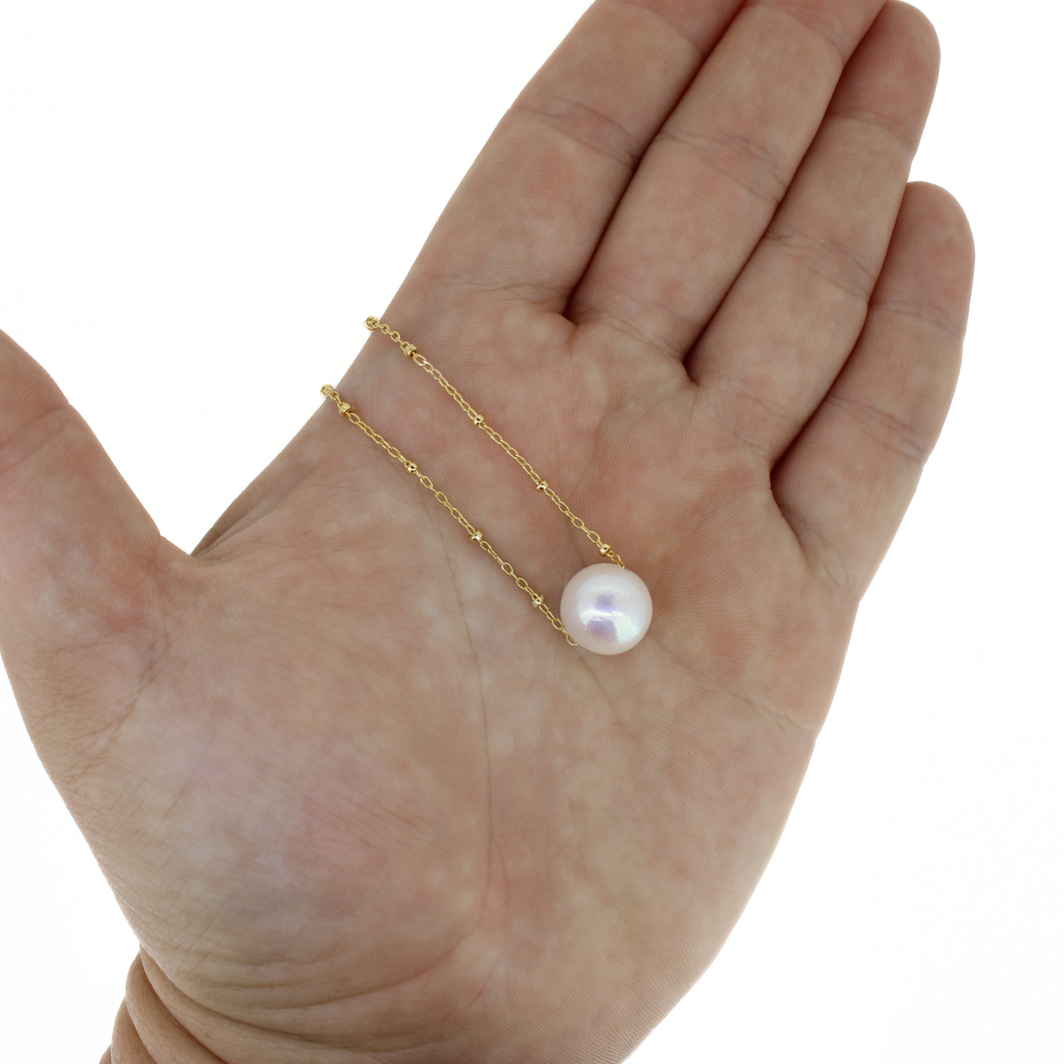 A delicate gold chain necklace with a single white freshwater pearl pendant, displayed on an open hand to show scale against a white background.
