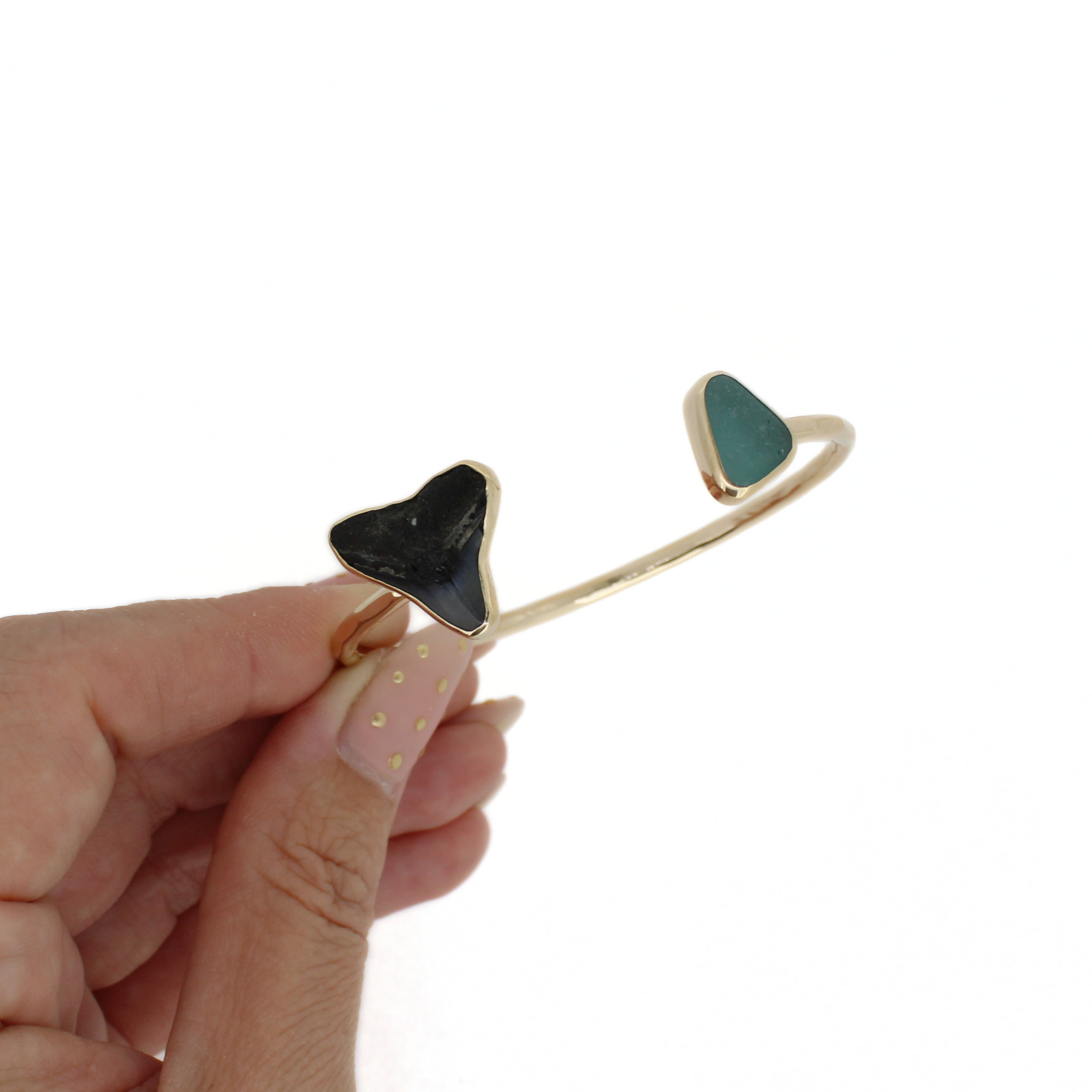 Gold cuff bracelet close-up with black shark tooth and green sea-glass triangle ends