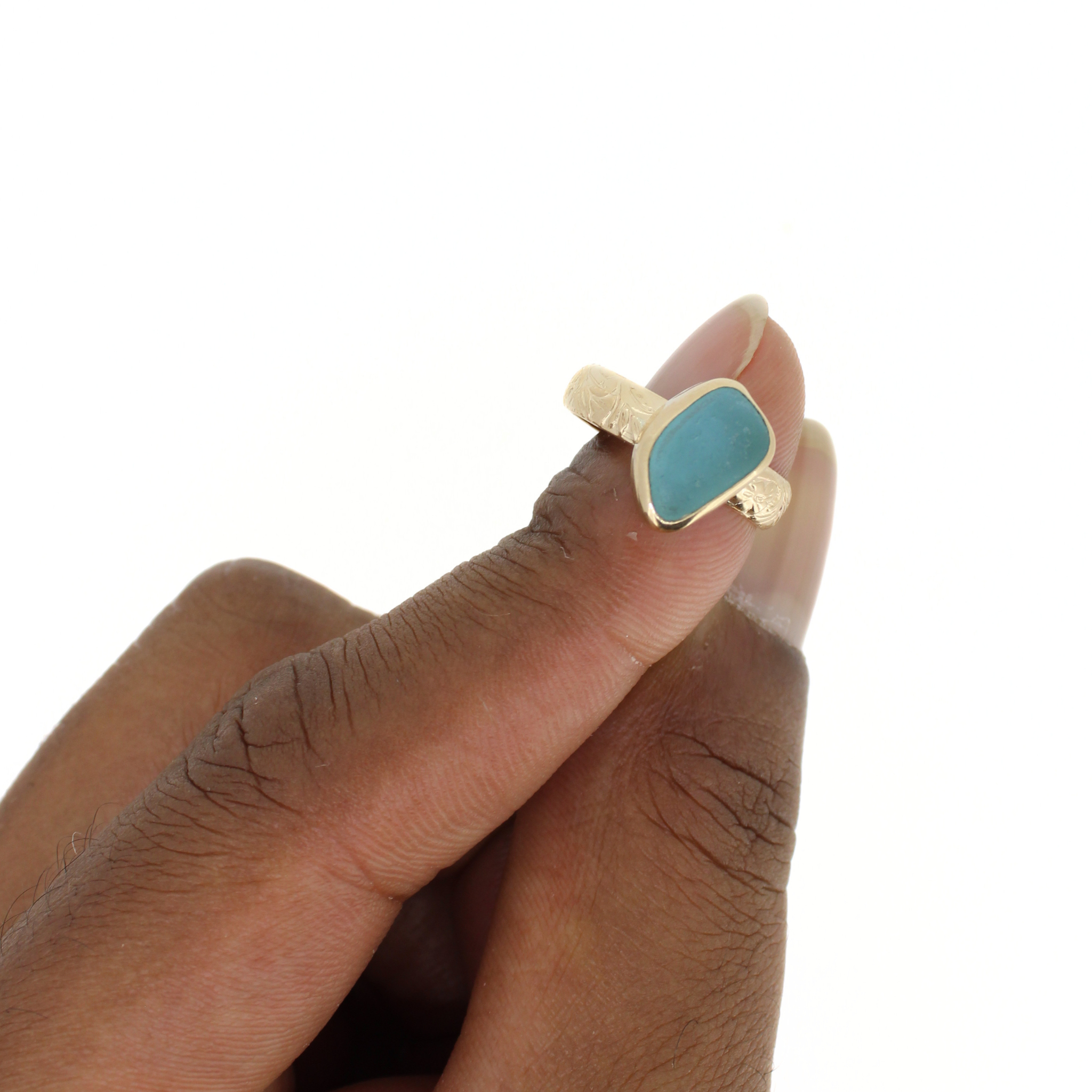 Gold-tone ring with teal sea-glass teardrop bezel seen from side on finger.