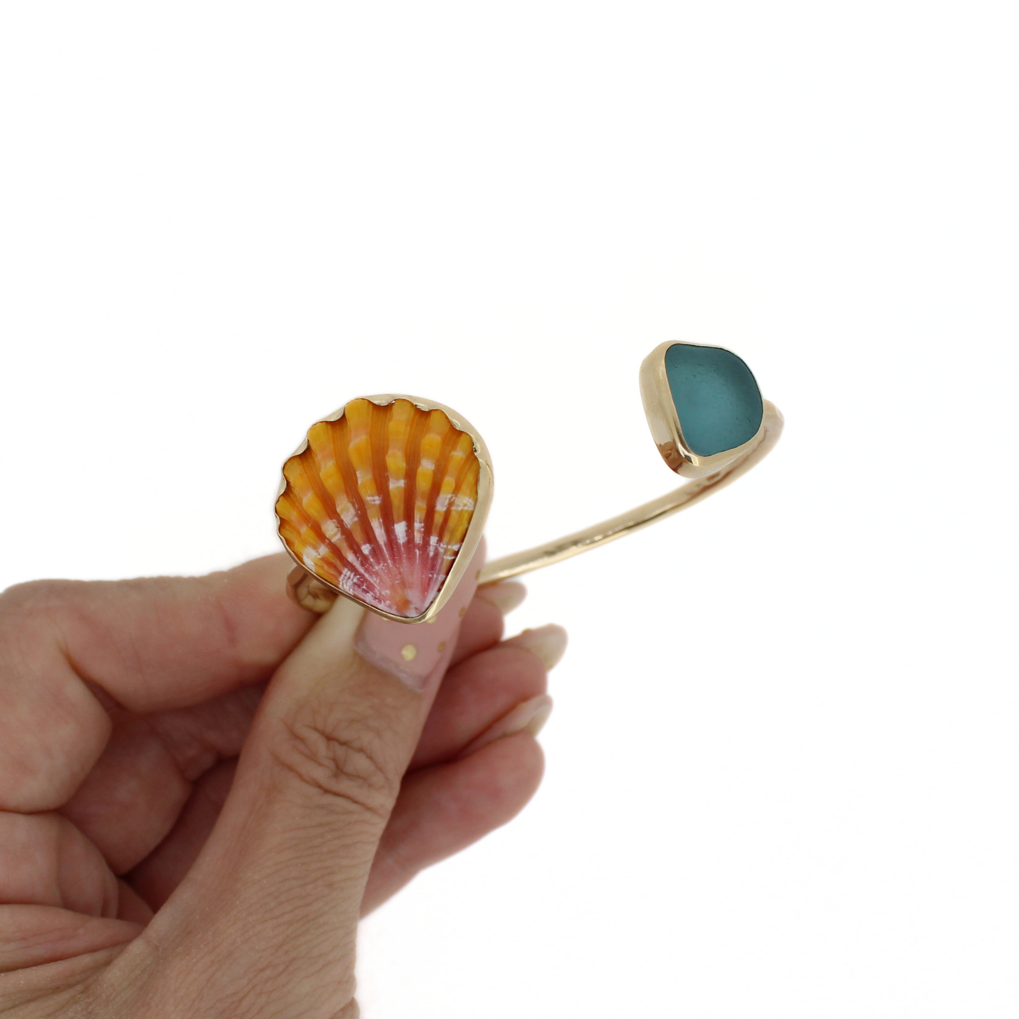 Gold cuff bracelet detail: orange sunrise shell charm with teal sea-glass square
