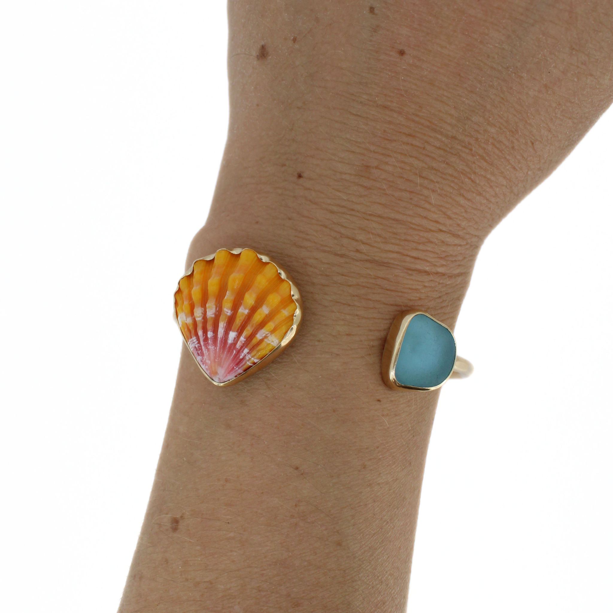 Gold cuff bracelet on wrist with teal sea-glass square and orange sunrise shell