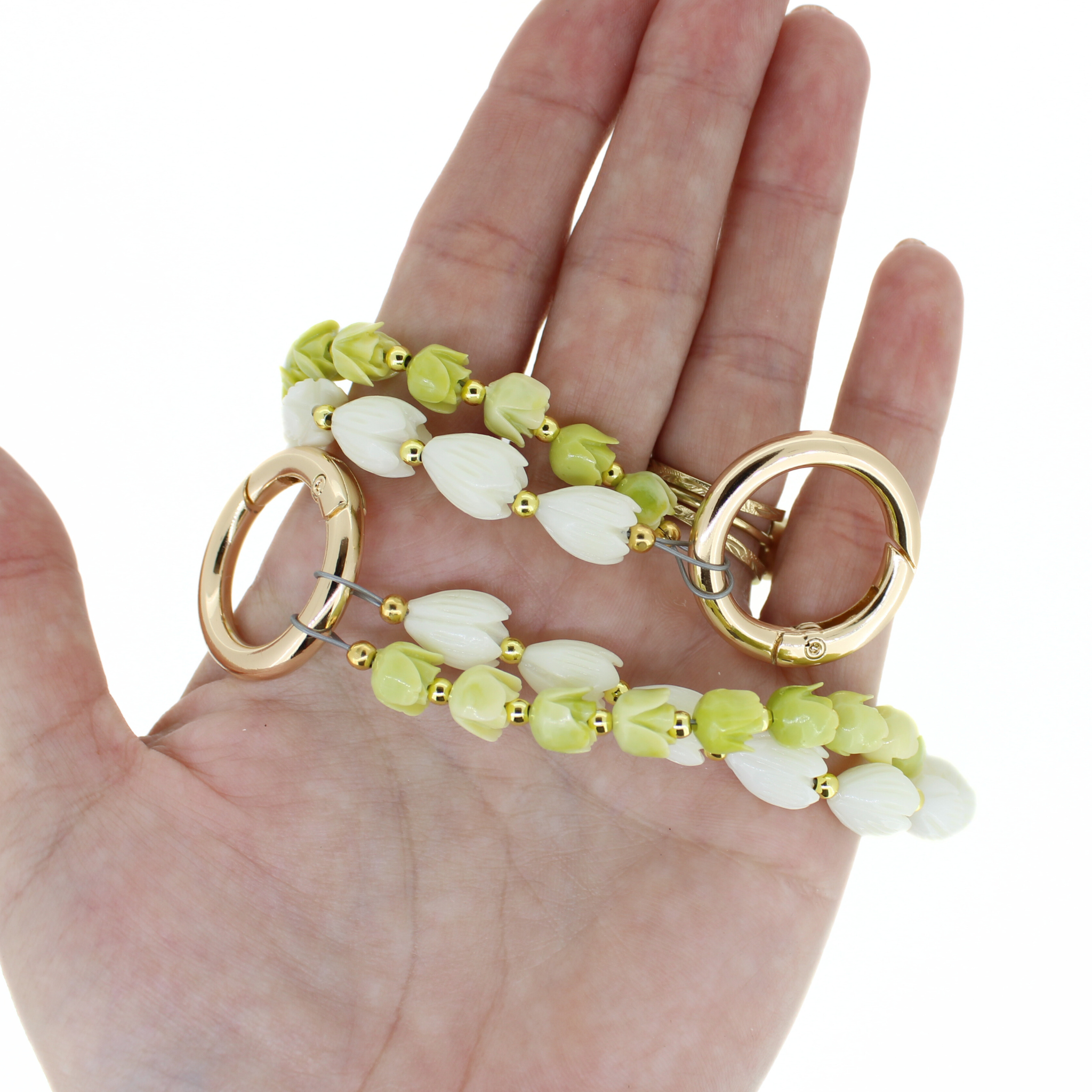 White and green blossom purse lei with gold-tone rings, held in an open hand