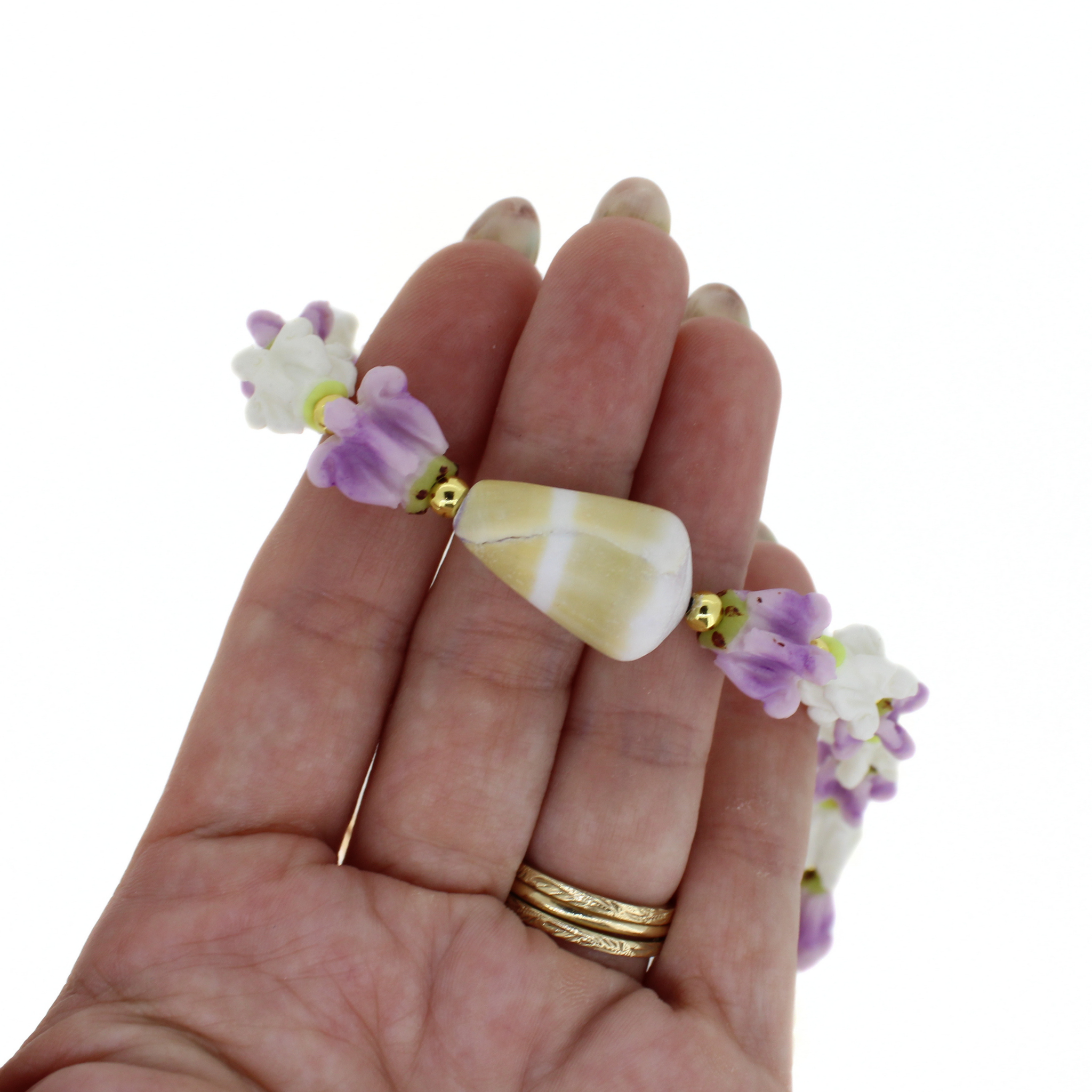 Beaded lei strand with purple flowers, white shells, and cone shell centerpiece on hand