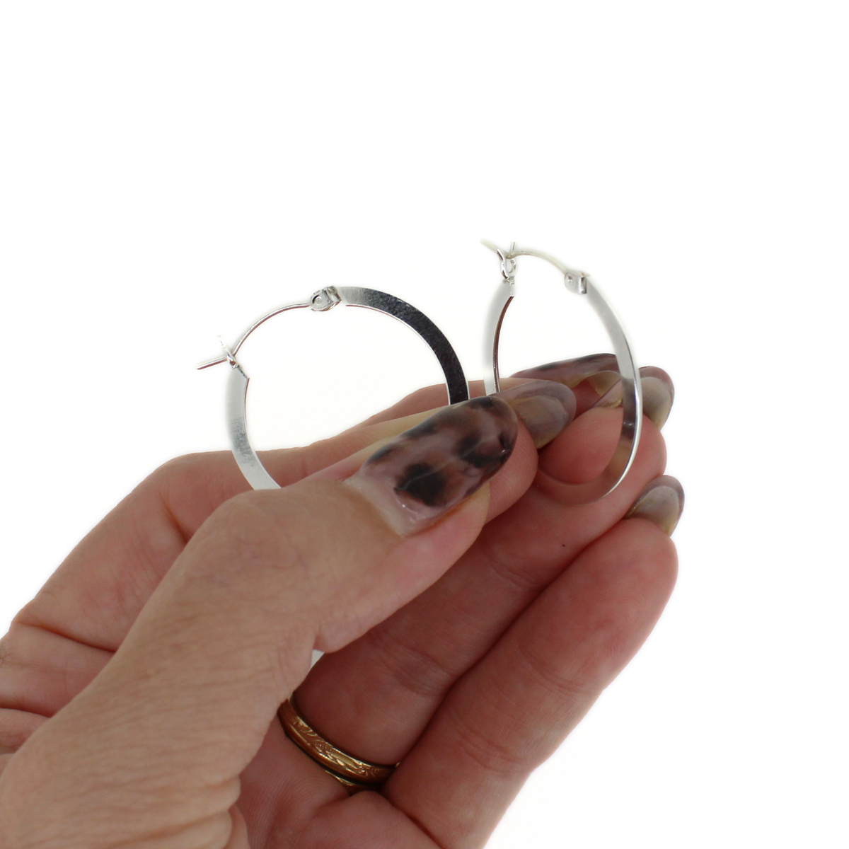 A pair of polished silver hoop earrings held between a person's fingers against a plain white background.