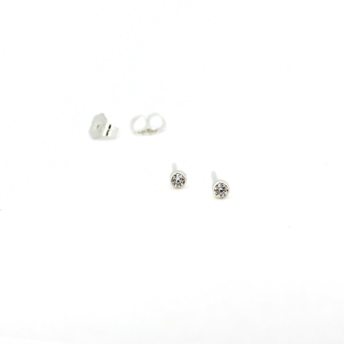 A pair of silver stud earrings with clear round gemstones, shown on a plain white background with one earring displaying its butterfly backing.