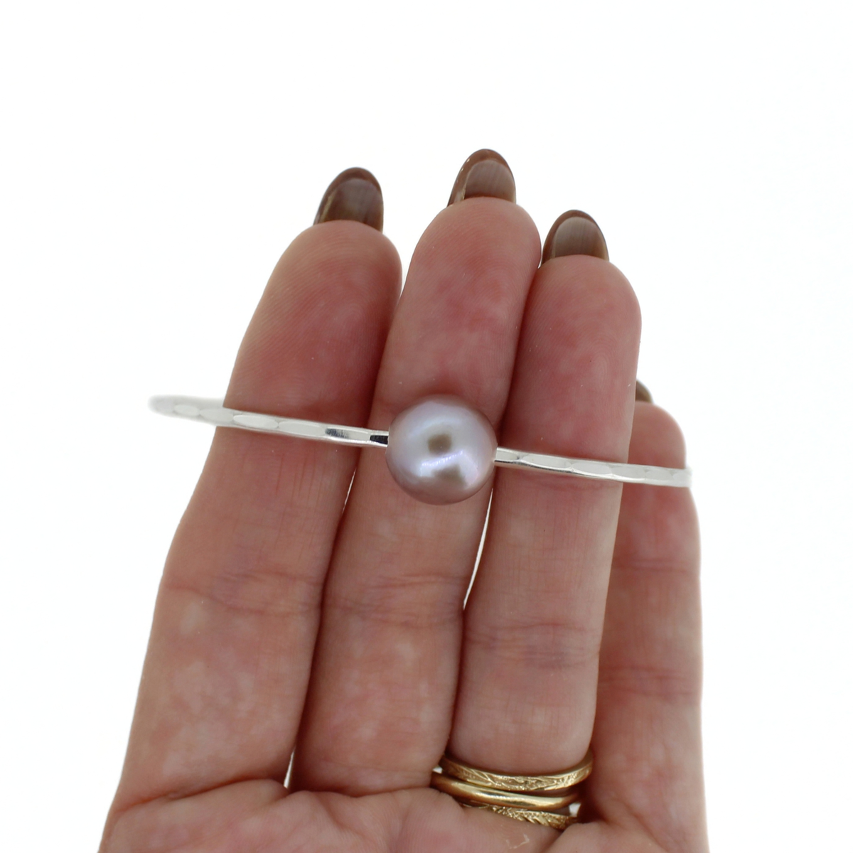 Silver bangle bracelet with a light purple pearl shown on a hand for size reference 