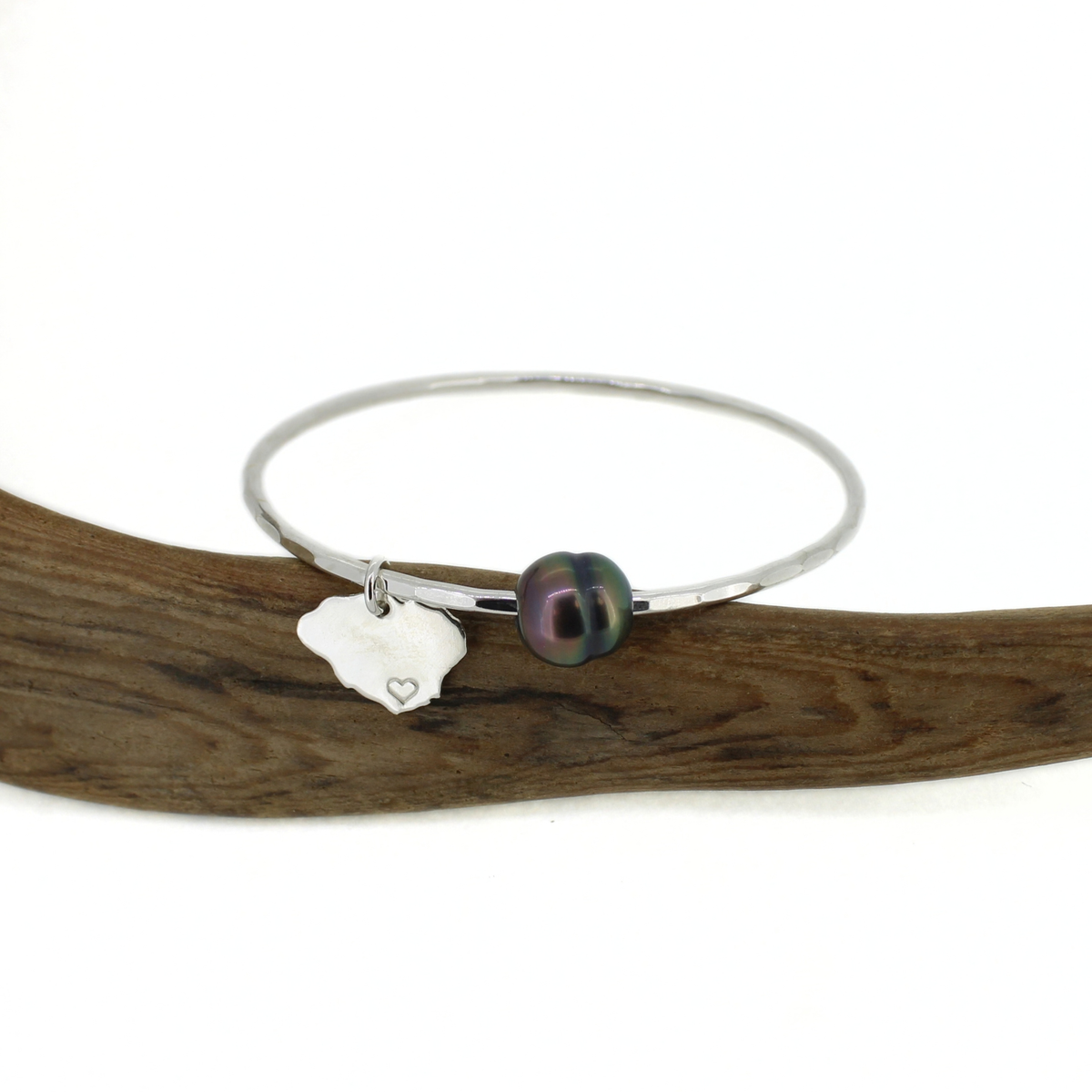 Sterling silver bangle bracelet with Tahitian pearl and Kauai island charm displayed on a piece of driftwood
