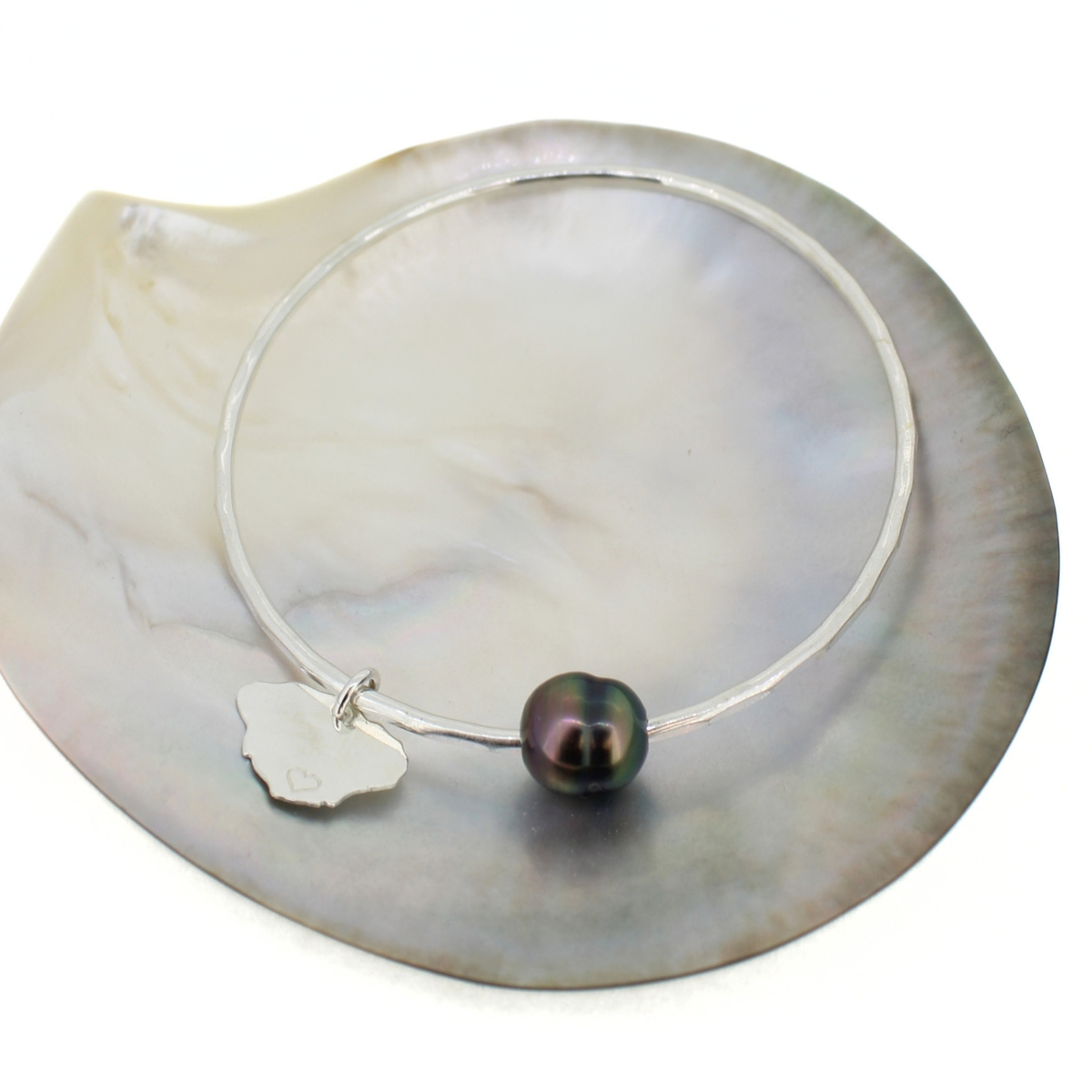 Sterling silver bangle bracelet with a Tahitian pearl and Kauai charm displayed on a mother of pearl shell