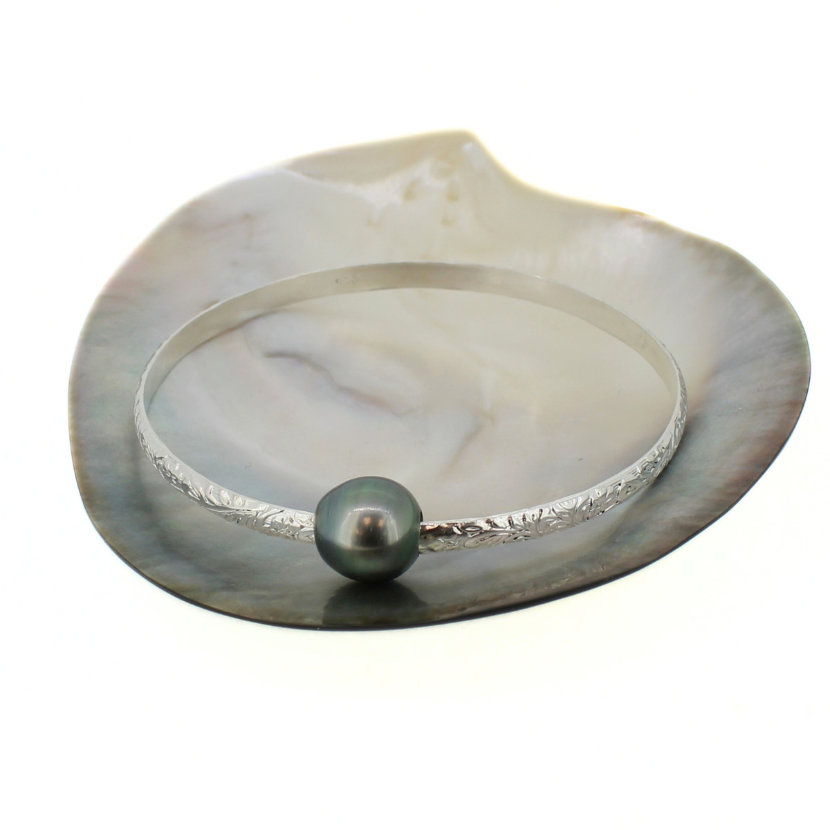 Sterling silver floral printed bangle bracelet with a dark Tahitian pearl, displayed on a shell against a white background