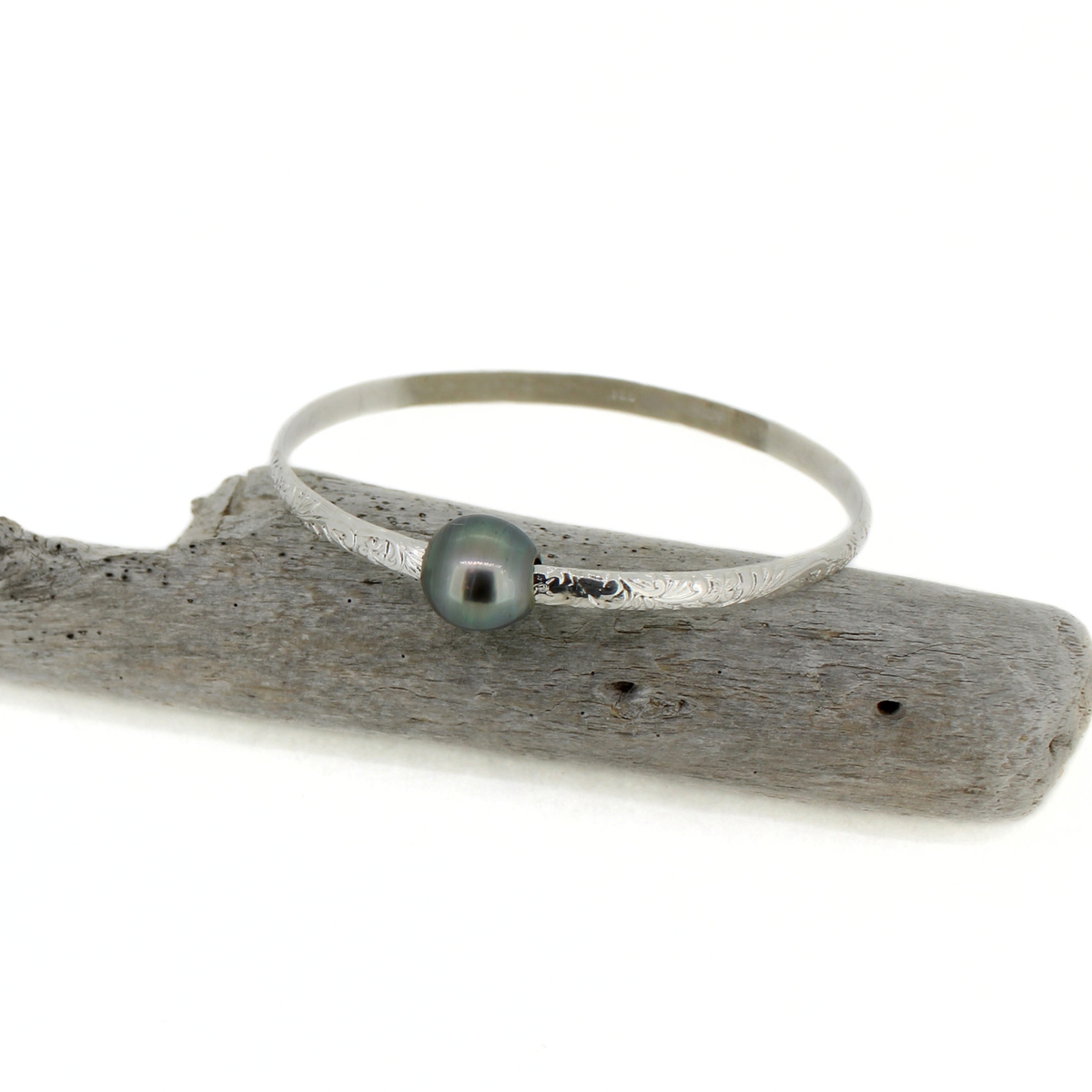 Silver bangle bracelet with Tahitian pearl displayed on a piece of driftwood