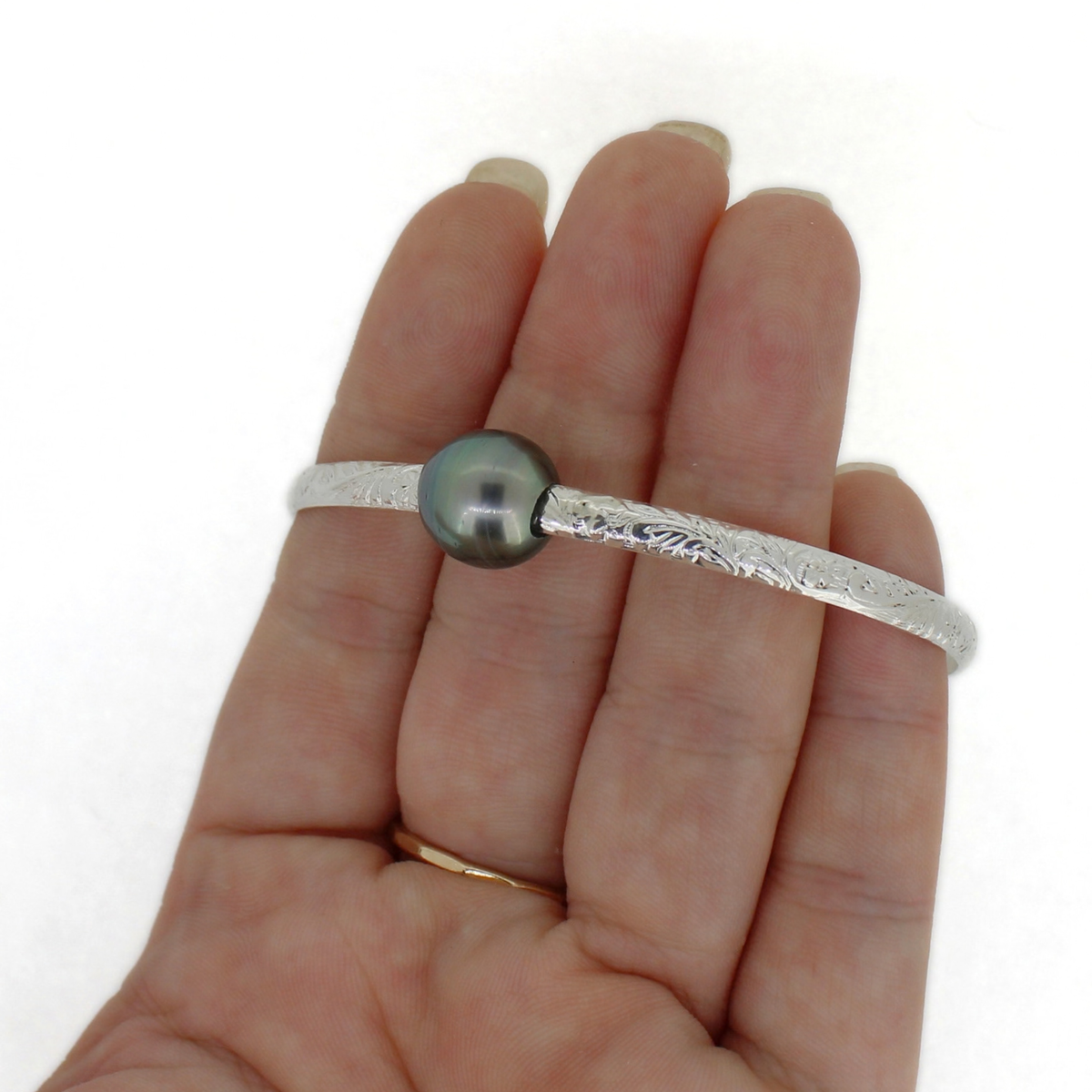 Silver floral printed bangle bracelet with dark gray Tahitian pearl on a persons fingers for size reference 