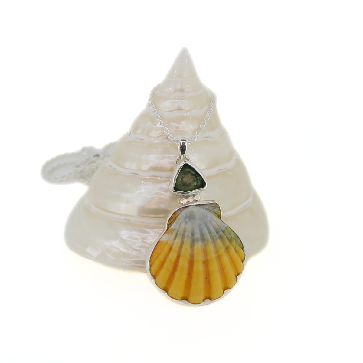 A silver necklace with a pendant featuring a yellow sunrise shell and a dark blue triangular stone, displayed on a white seashell stand against a white background.