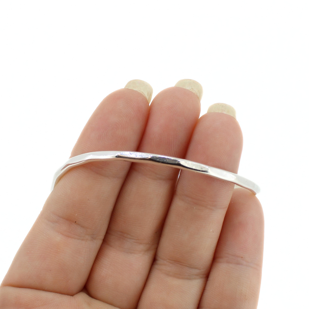 A thin, polished silver cuff bracelet held on a person's fingers against a plain white background.