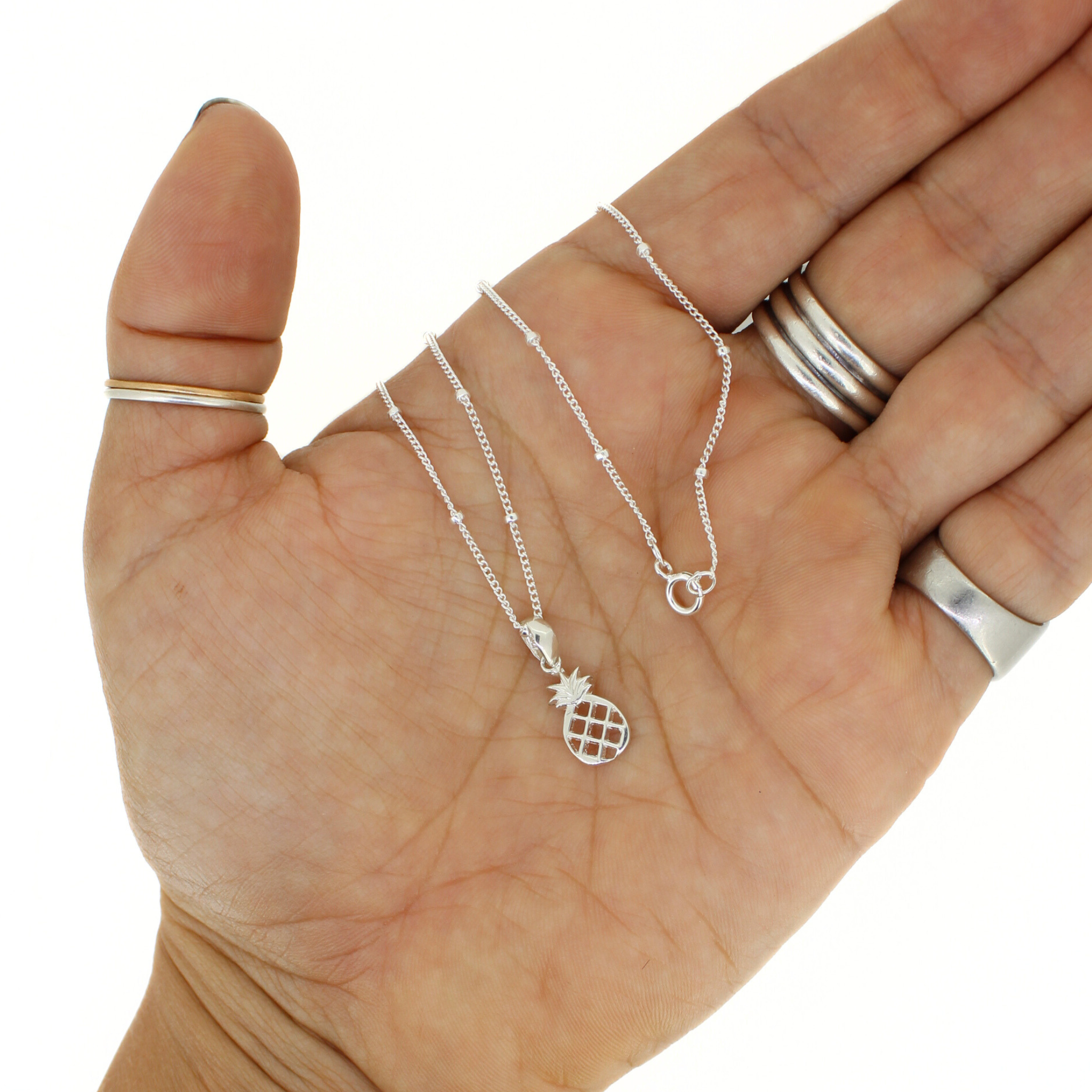 Silver pineapple pendant necklace on a hand for size reference with a white background