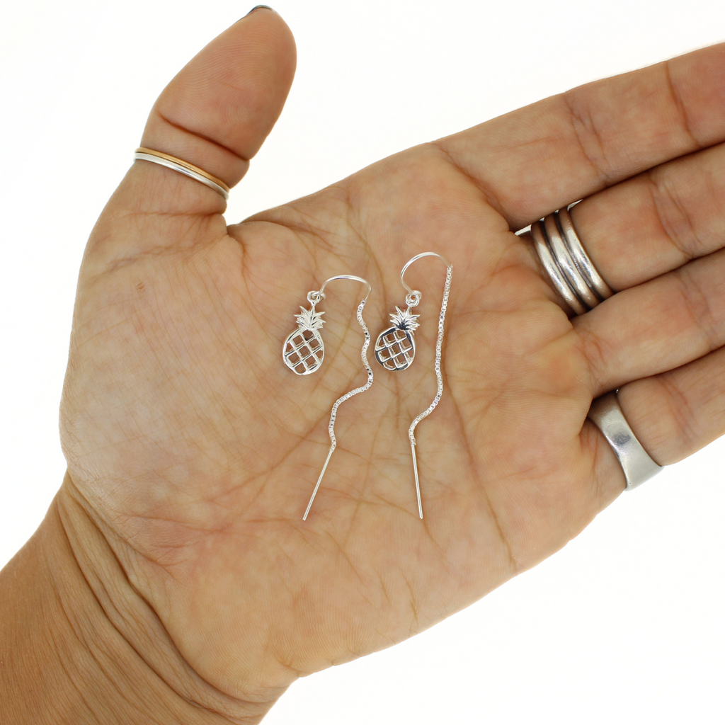 Silver pineapple-shaped earrings held in a hand with a white background