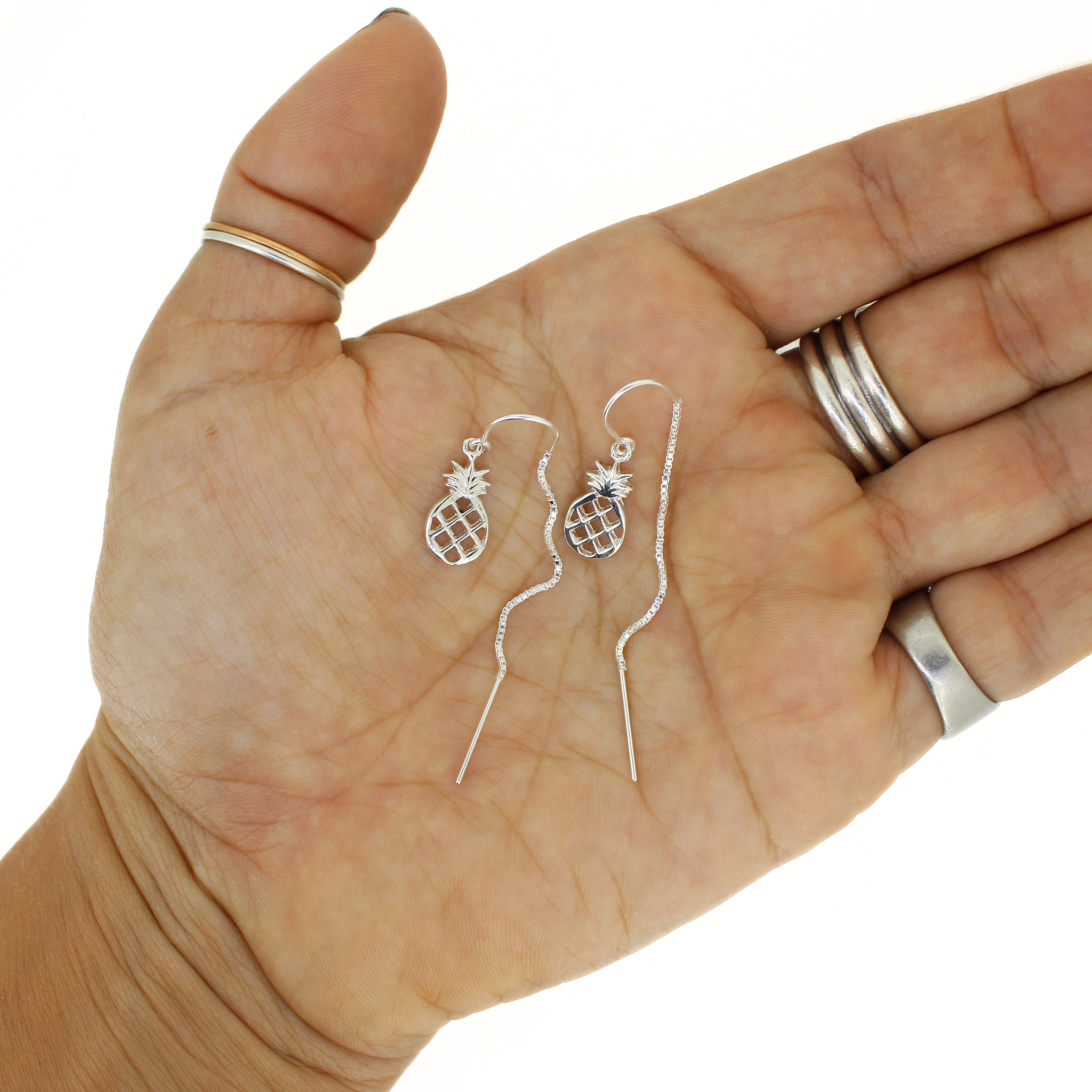 Silver pineapple-shaped earrings held in a hand with a white background