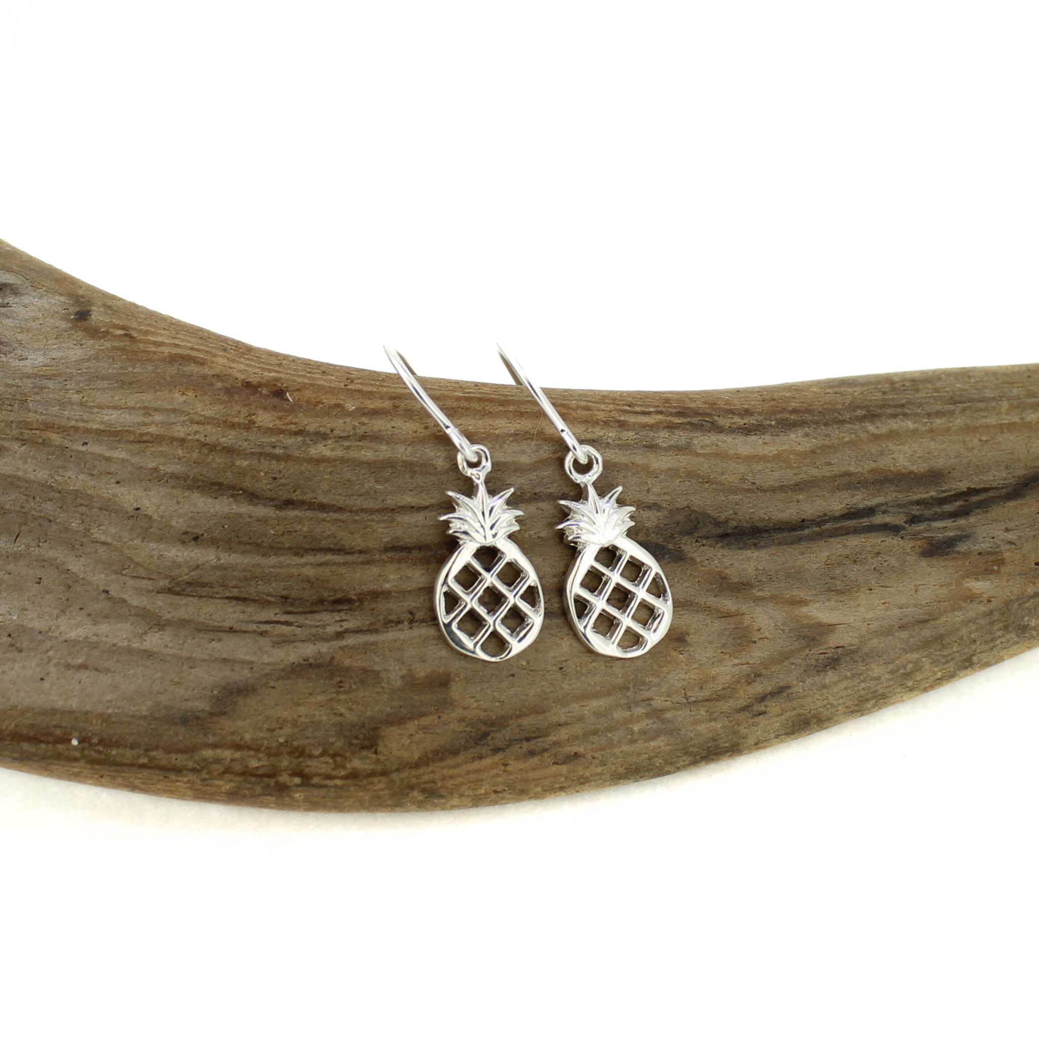 Silver pineapple earrings on a piece of driftwood
