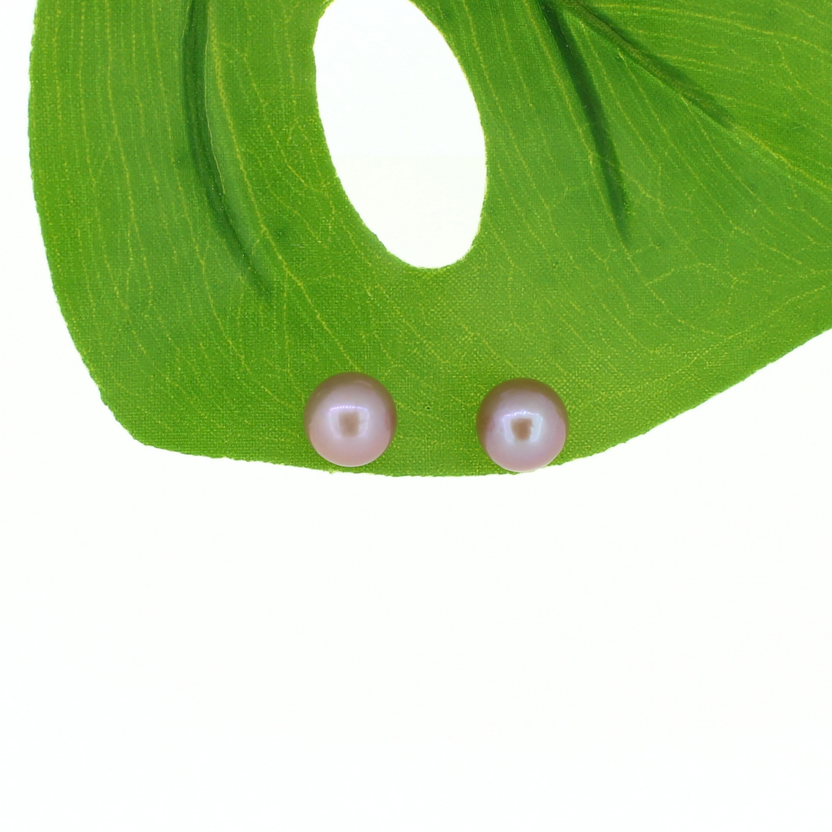 Two round pearl stud earrings with a soft pinkish-white luster, displayed on a bright green leaf against a white background.