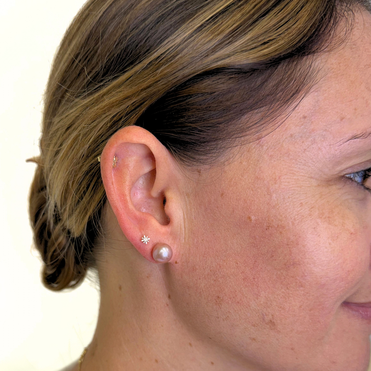 Close-up of a woman's ear wearing two small silver earrings: a star-shaped stud and a pearl stud, against a plain light background.
