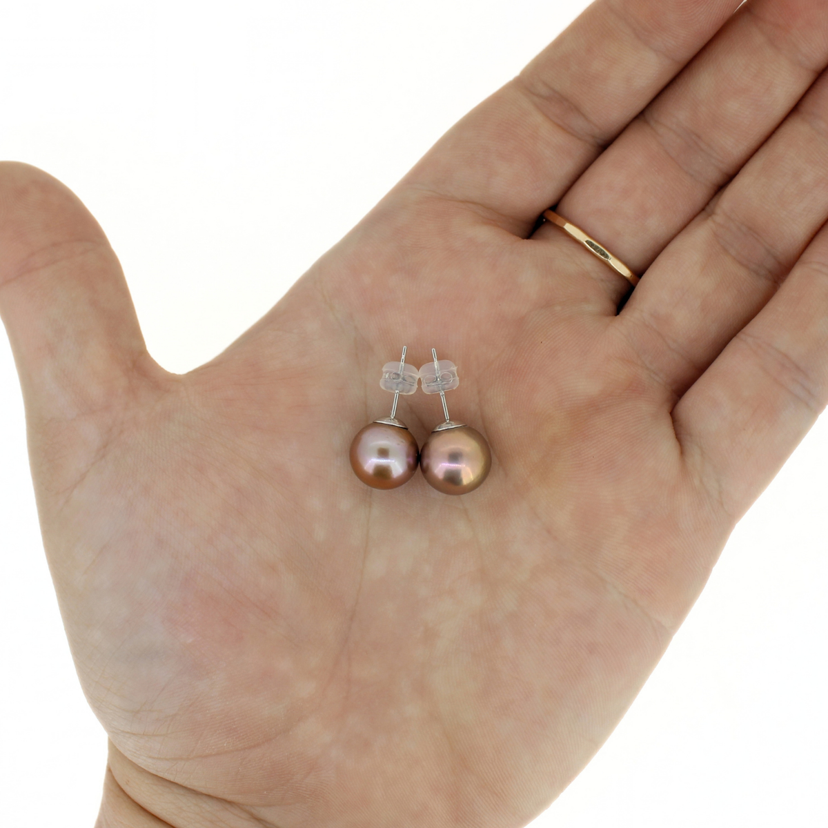 A pair of small drop earrings with iridescent brownish-pink freshwater pearls on silver posts, shown resting on an open hand against a white background.