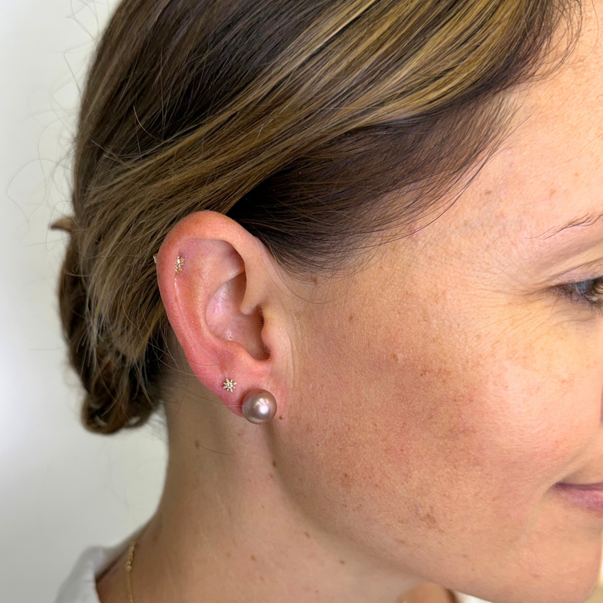 Close-up of a woman's ear wearing multiple small earrings, including a pearl stud and several star-shaped studs, against a plain light background.