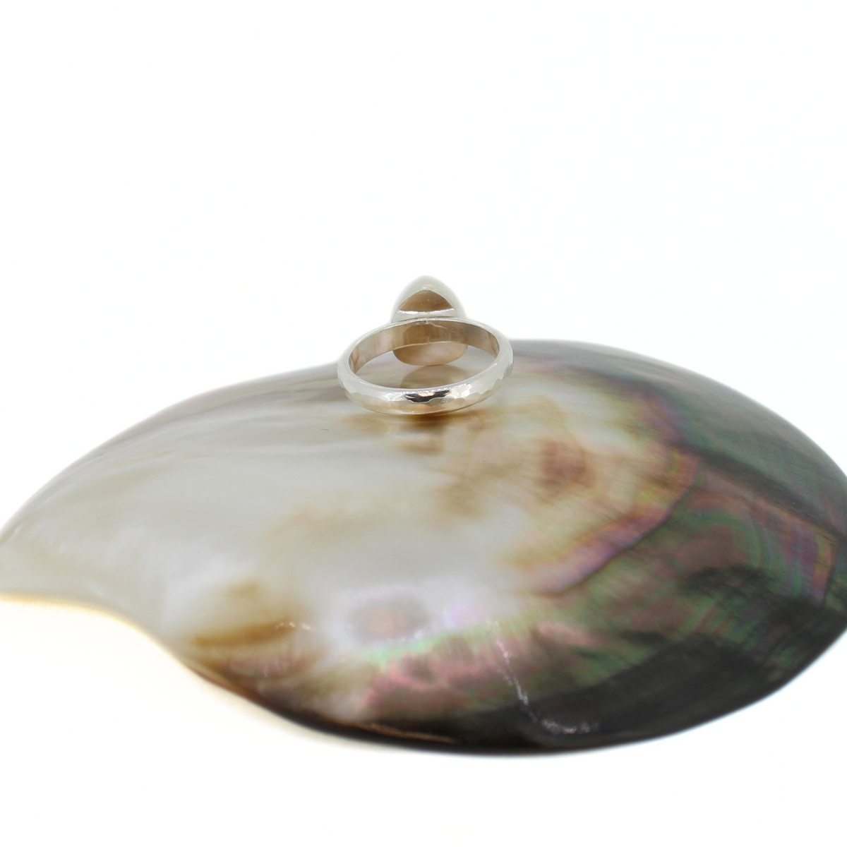 A sterling silver ring with a hammered band, displayed on top of an open iridescent shell against a plain white background.