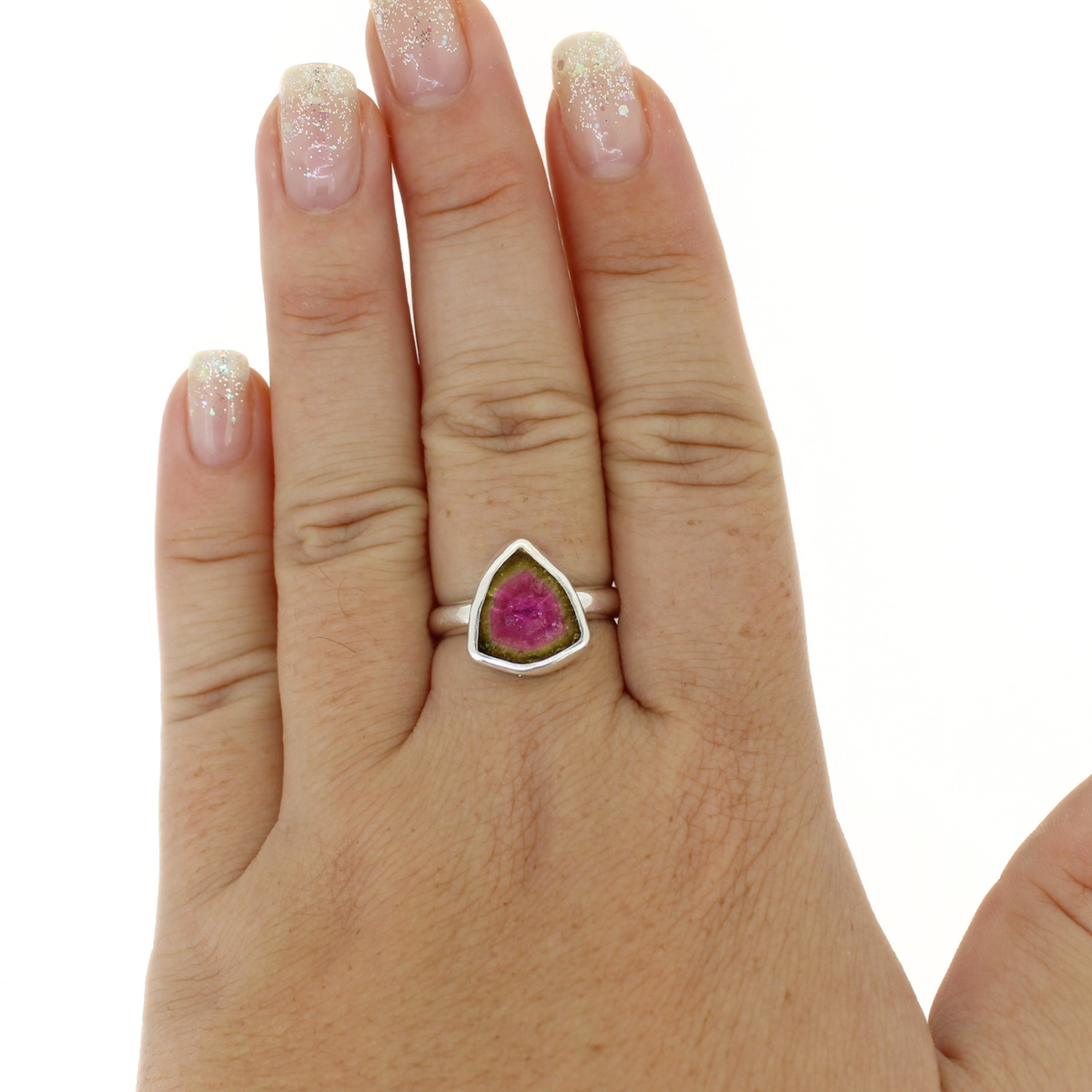 A hand wearing a silver ring with a triangular pink and green watermelon tourmaline gemstone, shown against a plain white background.