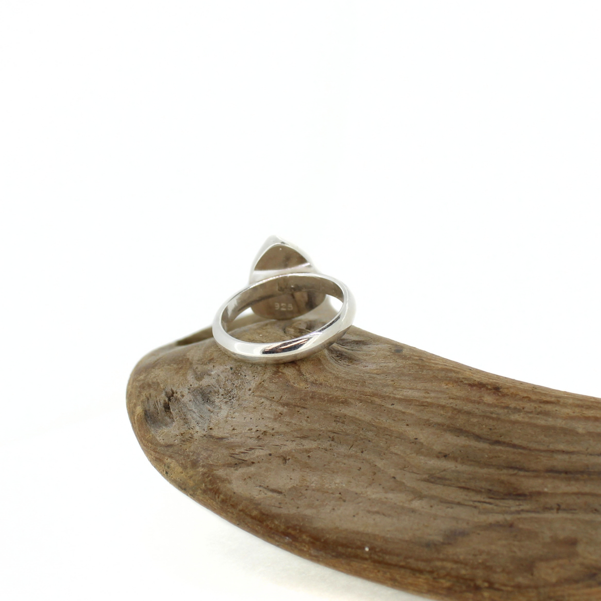A polished silver ring with a triangular stone, displayed on a curved piece of natural wood against a white background.