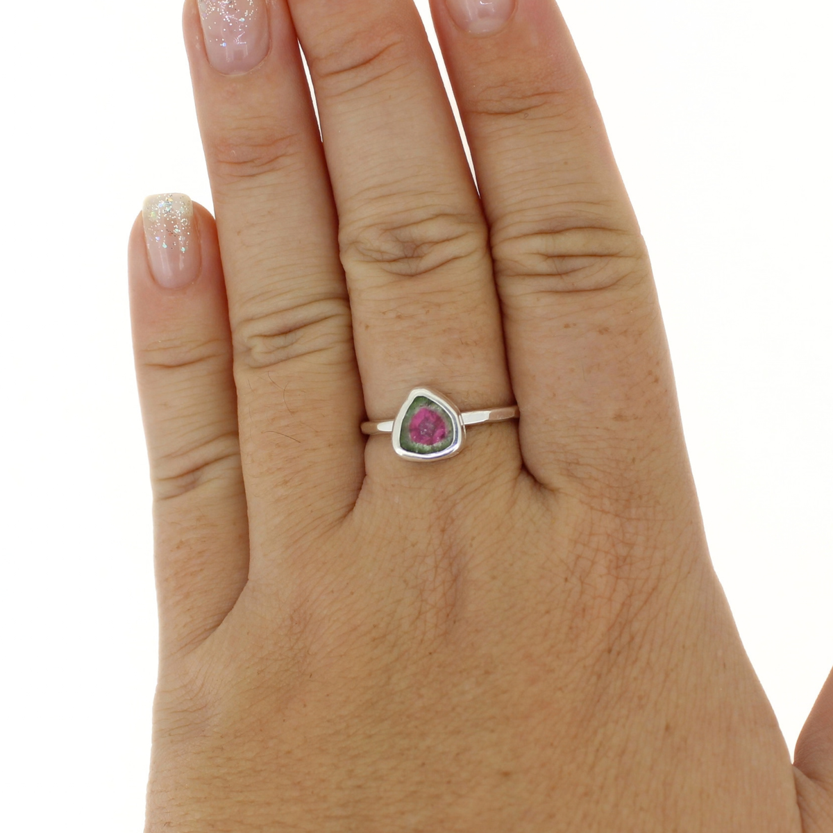 A silver ring with a triangular pink and green gemstone, worn on a person's ring finger against a plain white background.
