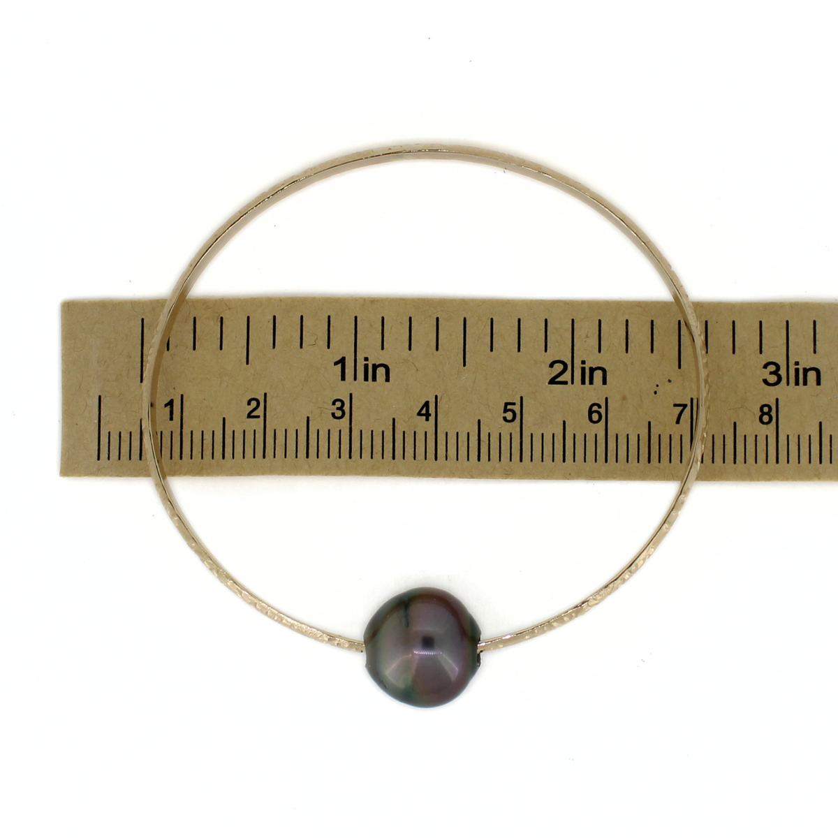 Gold oval shaped pearl bangle over a ruler for size reference 