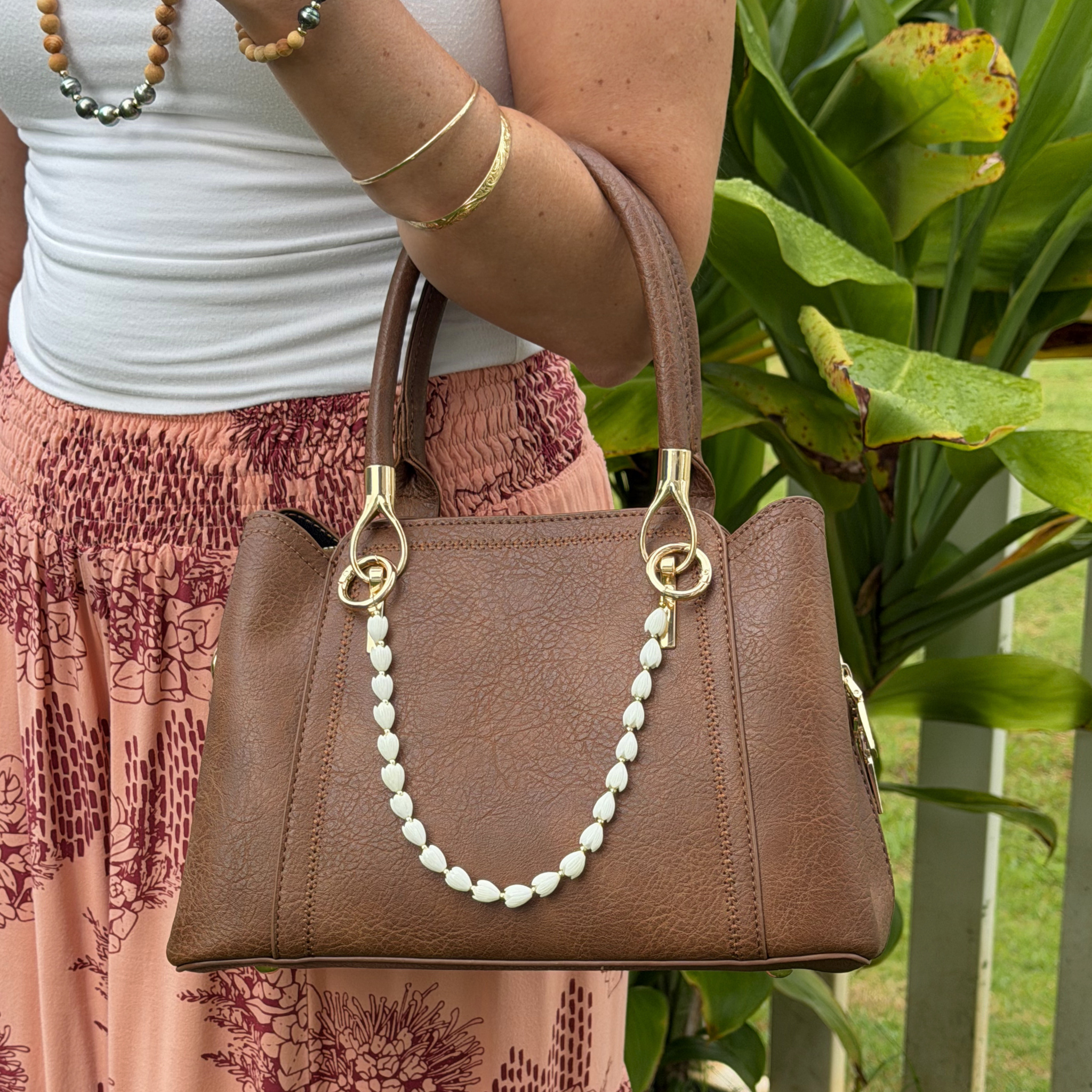 Flower purse lei on a brown handbag strap: white petal beads with gold-tone rings