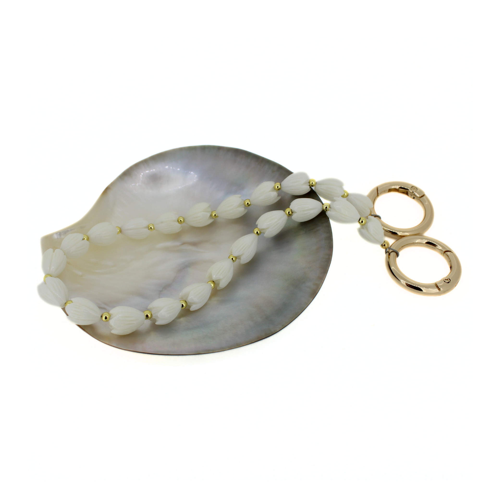 Flower purse lei laid on an oval shell dish: white petal beads, small gold accents, rings