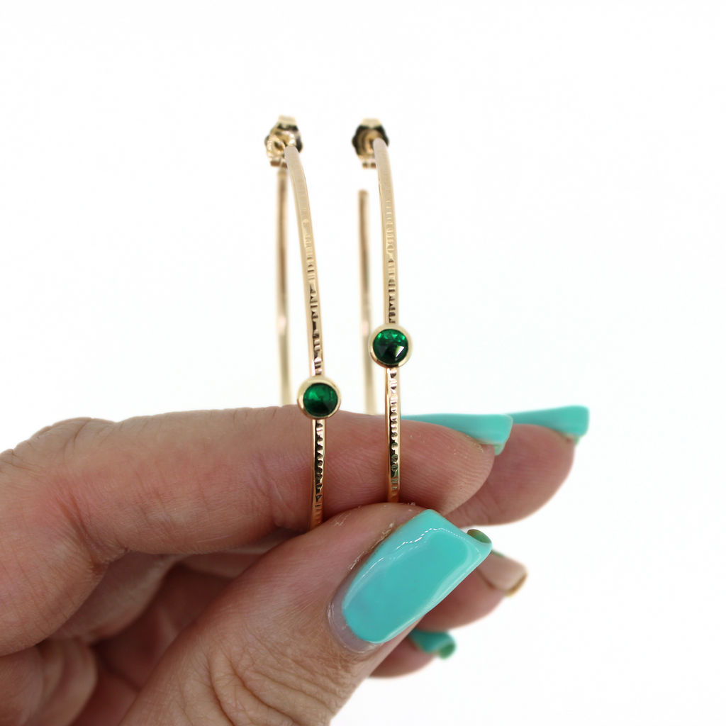 Brianne and Company hand forged hammered hoop gold earrings with bezel set emeralds for May birthday
