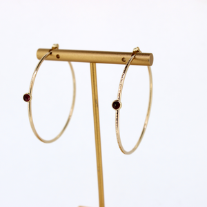 Brianne & Co gold hammered hoops with bezel set ruby shown on earring display