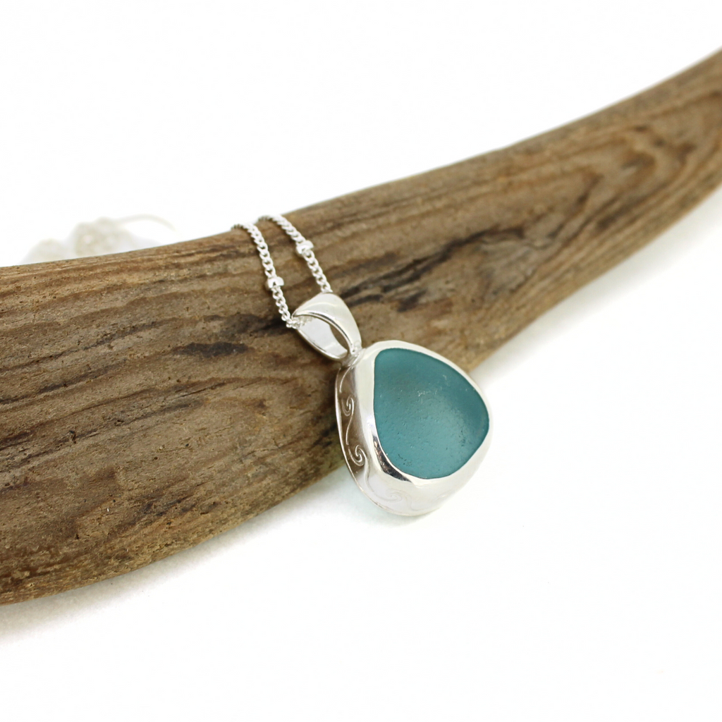 Brianne and Company Sterling Silver Blue Sea Glass Necklace w/ Wave Design on a piece of wood