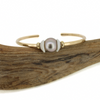 Brianne and Co gold fill tahitian pearl and puka shell cuff on a piece of wood