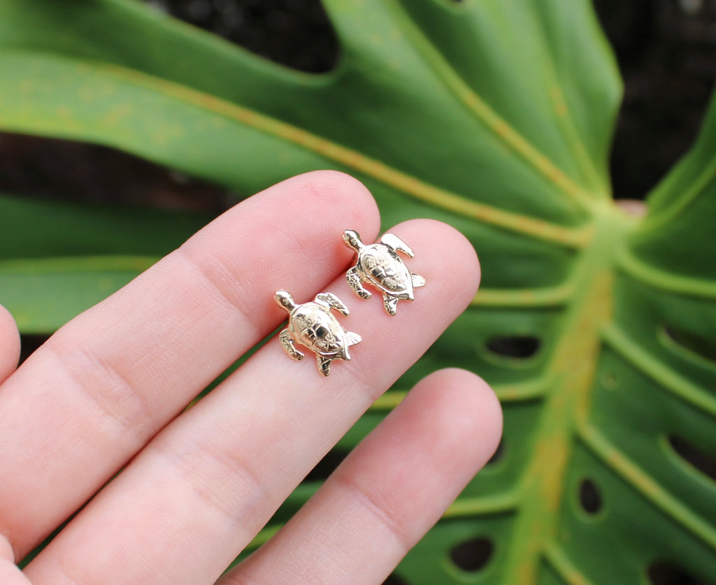 Brianne & Co. 14k yellow gold small turtle honu stud earrings between fingers for size reference